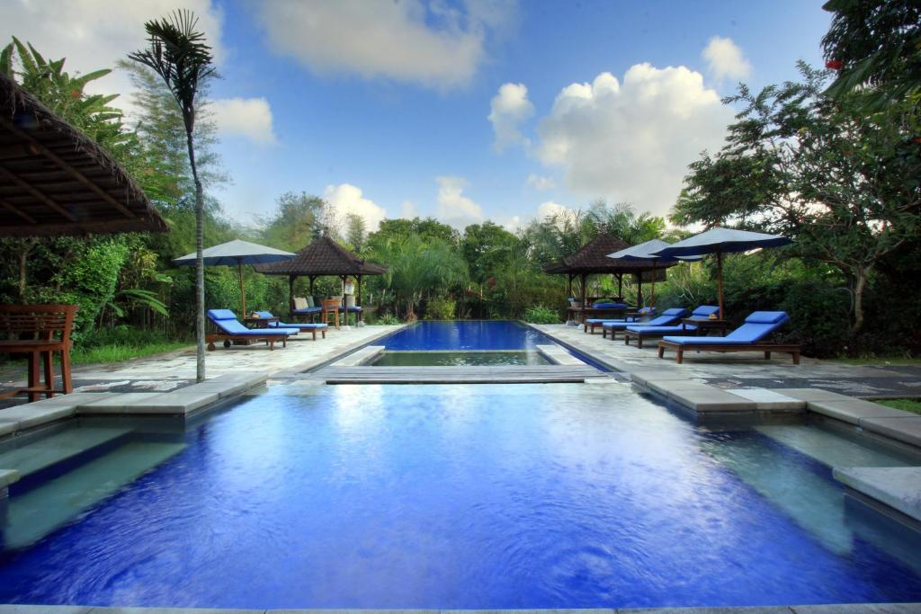a large swimming pool with chairs and umbrellas at Nara Ubud Cottage by Mahaputra in Ubud