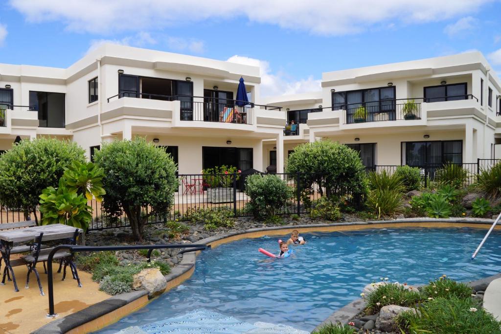 a family swimming in a swimming pool in front of a house at Ocean Breeze Resort Pauanui in Pauanui
