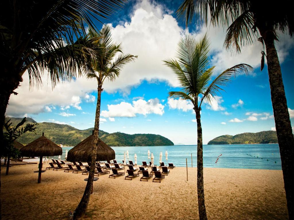 a beach with chairs and umbrellas and the ocean at Costa Verde Tabatinga Hotel in Caraguatatuba