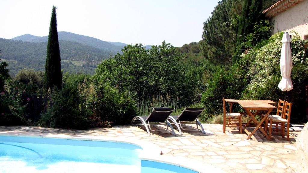 un patio con mesa y sillas junto a una piscina en Appartement avec piscine chauffée, en Collobrières