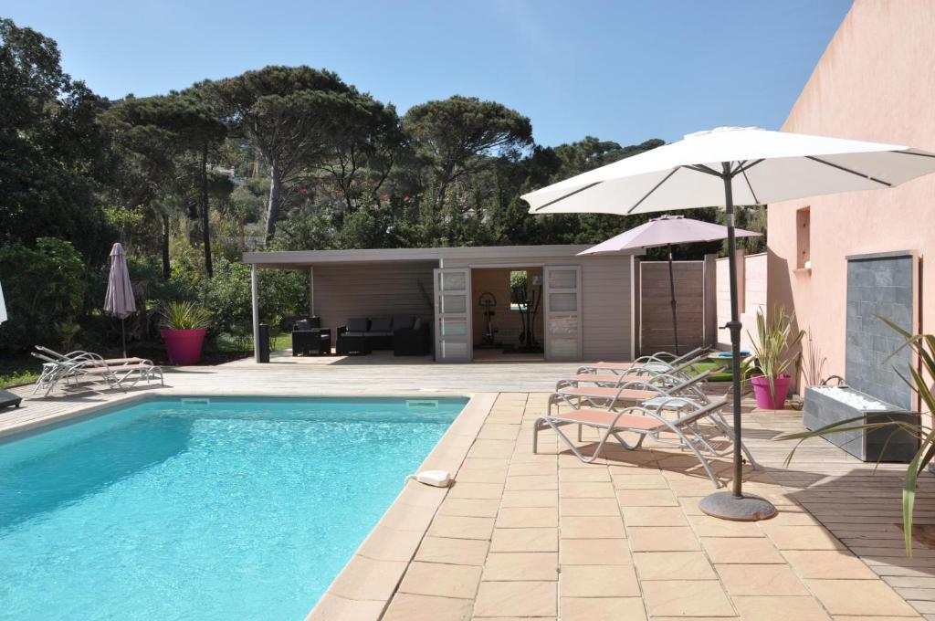 una casa y una piscina con sombrilla y sillas en Hôtel de la Vierge Noire en Sainte-Maxime