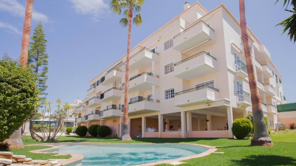 a large white building with palm trees and a swimming pool at Apartamentos Quinta da Praia in Alvor
