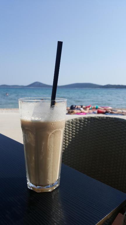 a drink sitting on a table next to the beach at Apartmani Adriana1979 in Vodice