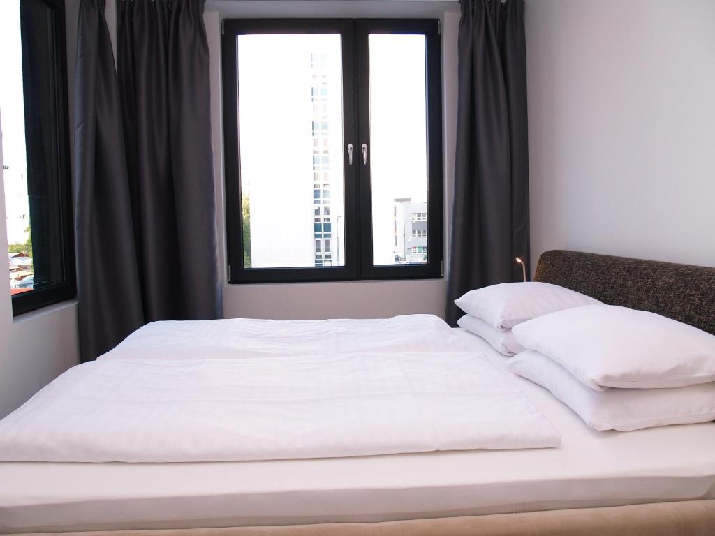 un letto con lenzuola e cuscini bianchi in una stanza con finestre di Elegant Apartment Miletičova, Free Parking a Bratislava