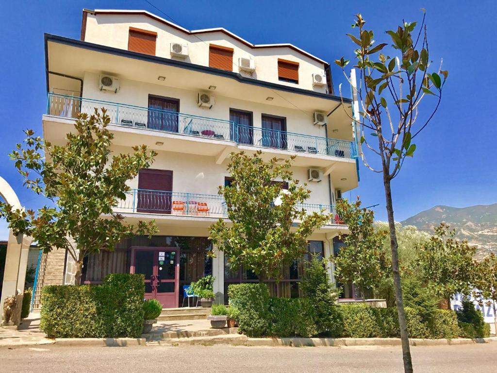 un edificio blanco con árboles delante de él en RAMIS Hotel & Outdoor Sports Center, en Përmet