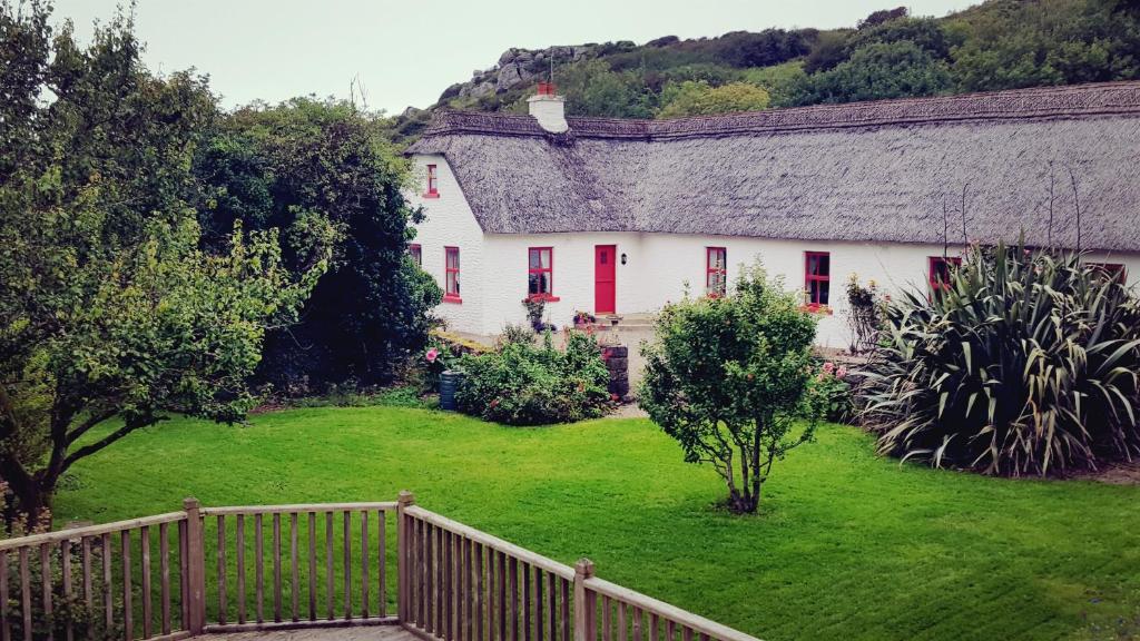 ein weißes Haus mit roten Rollläden und einem grünen Hof in der Unterkunft Rose Cottage in Doolin