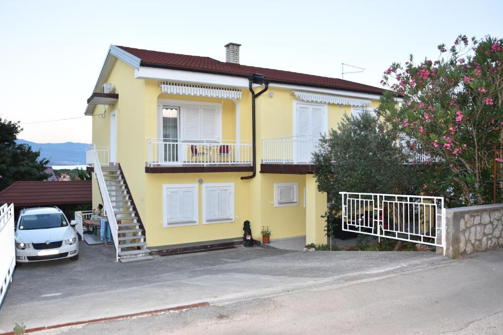 żółty dom z samochodem zaparkowanym przed nim w obiekcie Apartmani Novosel w mieście Šilo