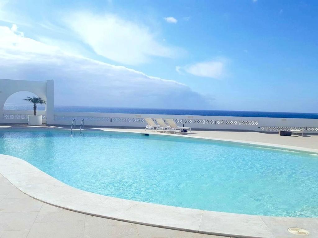 a swimming pool with chairs and the ocean in the background at Apartment Monte Del Moro in San Agustin