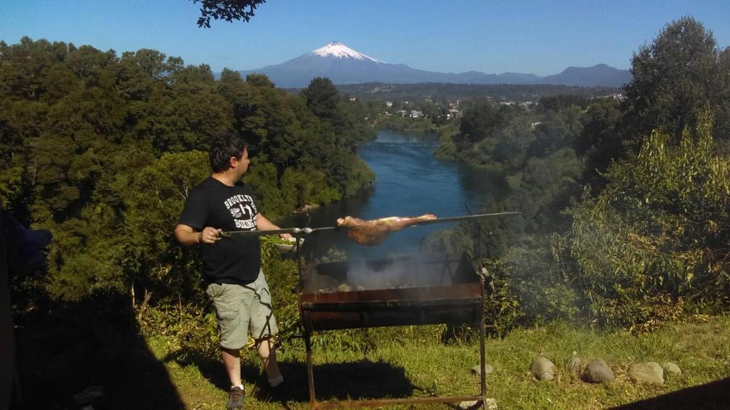 un hombre sosteniendo un palo con un pedazo de carne en Cabañas Portal del Rio, en Villarrica