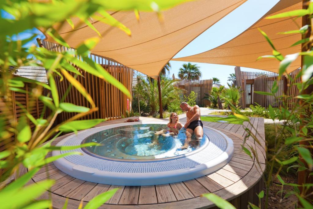 dos personas sentadas en una piscina bajo un paraguas en Mobil Homes Vacances en Grimaud