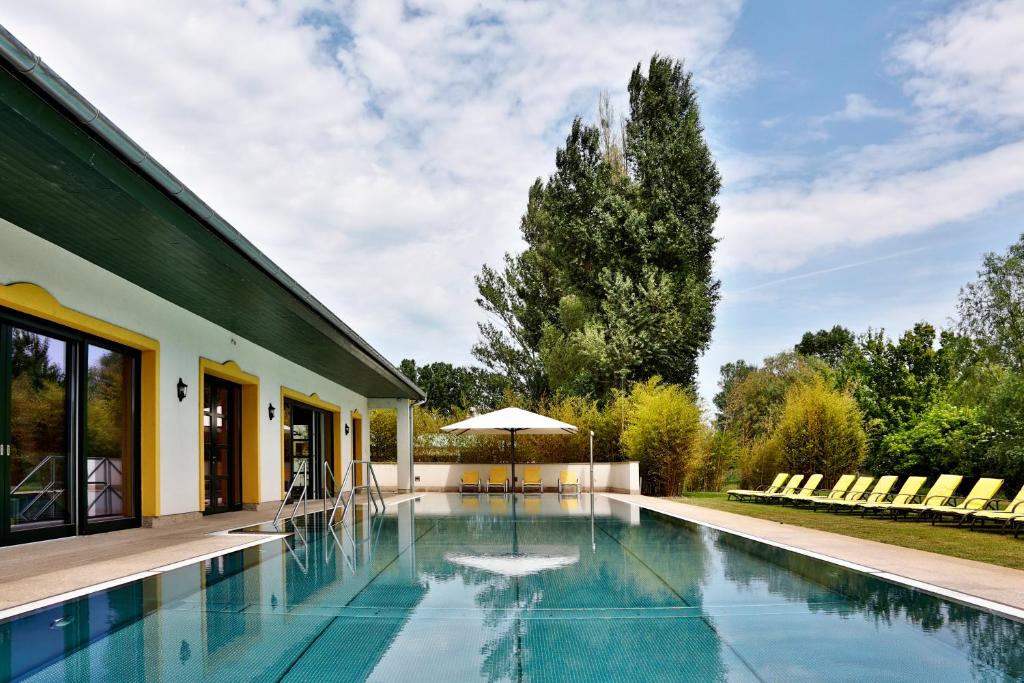einen Pool mit Sonnenschirm neben einem Haus in der Unterkunft Hubertus Hof Landhotel in Balatonfenyves