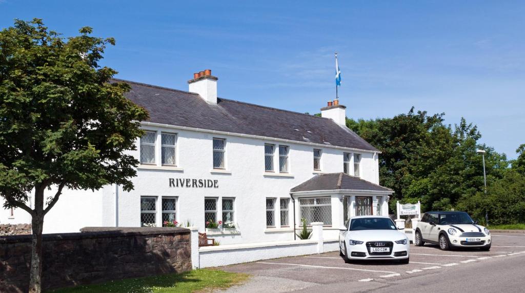 twee auto's geparkeerd voor een wit gebouw bij Riverside in Ullapool