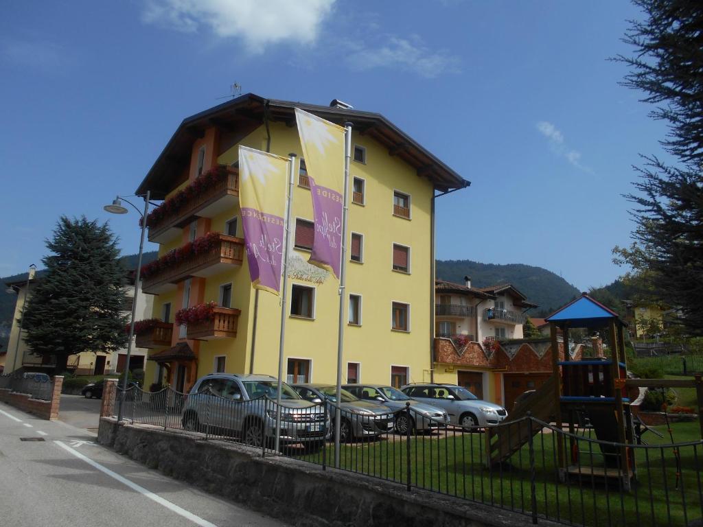 un bâtiment jaune avec des voitures garées devant lui dans l'établissement Residence Stella delle Alpi, à Cavedago