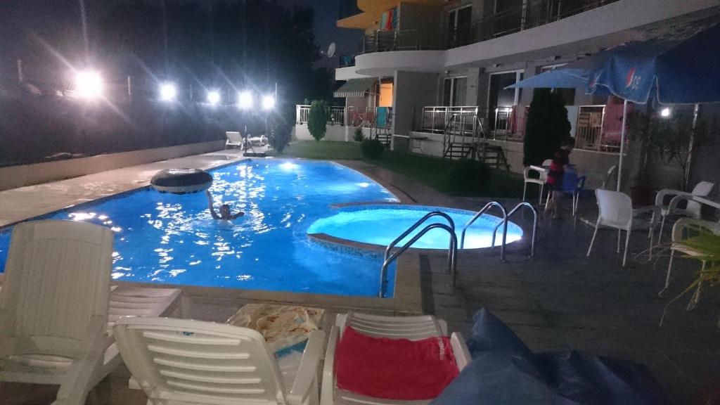 een groot zwembad 's nachts met stoelen en tafels bij Club Priz in Primorsko
