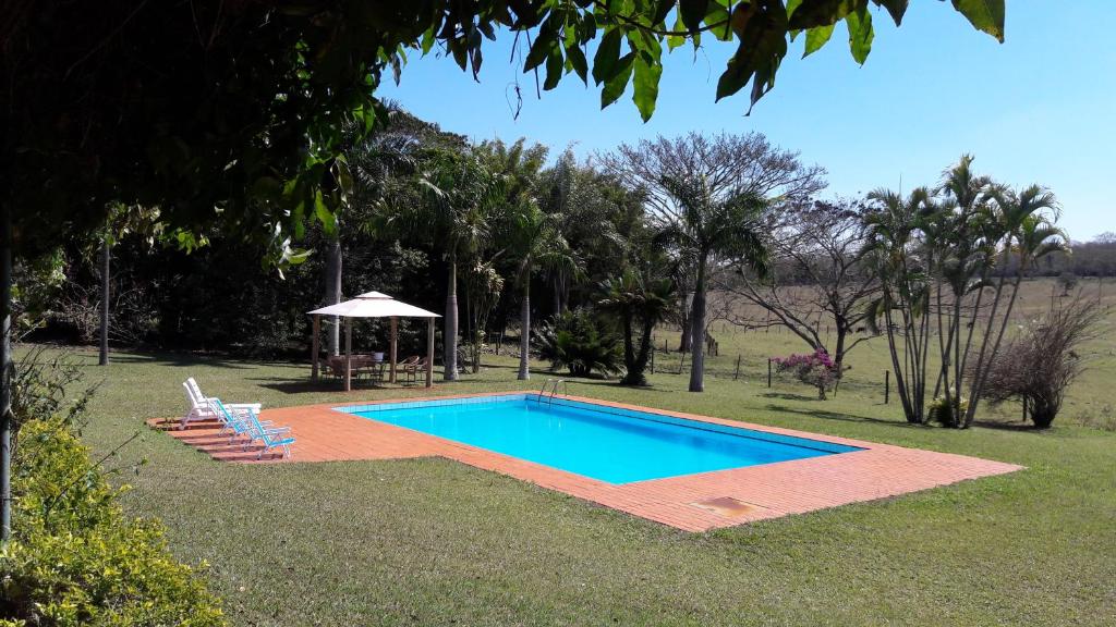 a swimming pool with two chairs and an umbrella at Chácara San Diego - Brotas in Brotas