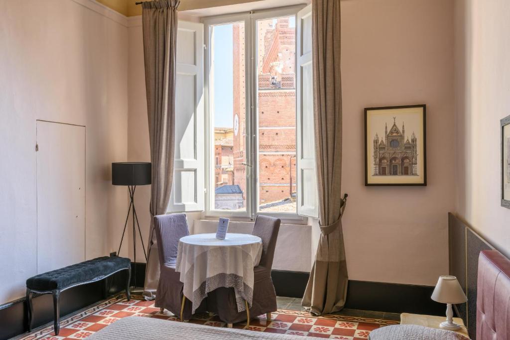 mesa y sillas en una habitación con ventana en La Terrazza Sul Campo-Rooms Only, en Siena