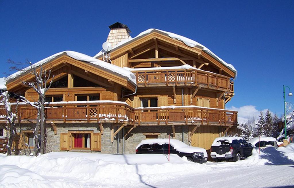 une grande maison en bois avec des voitures garées dans la neige dans l'établissement Odalys Chalet Levanna Occidentale, à Les Deux Alpes