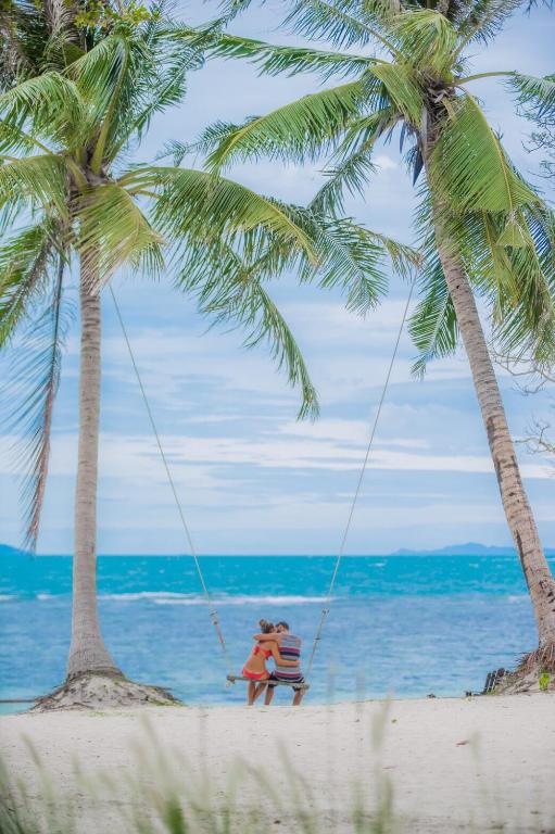 two people sitting in a swing on the beach at The Cabin Beach Resort in Haad Rin