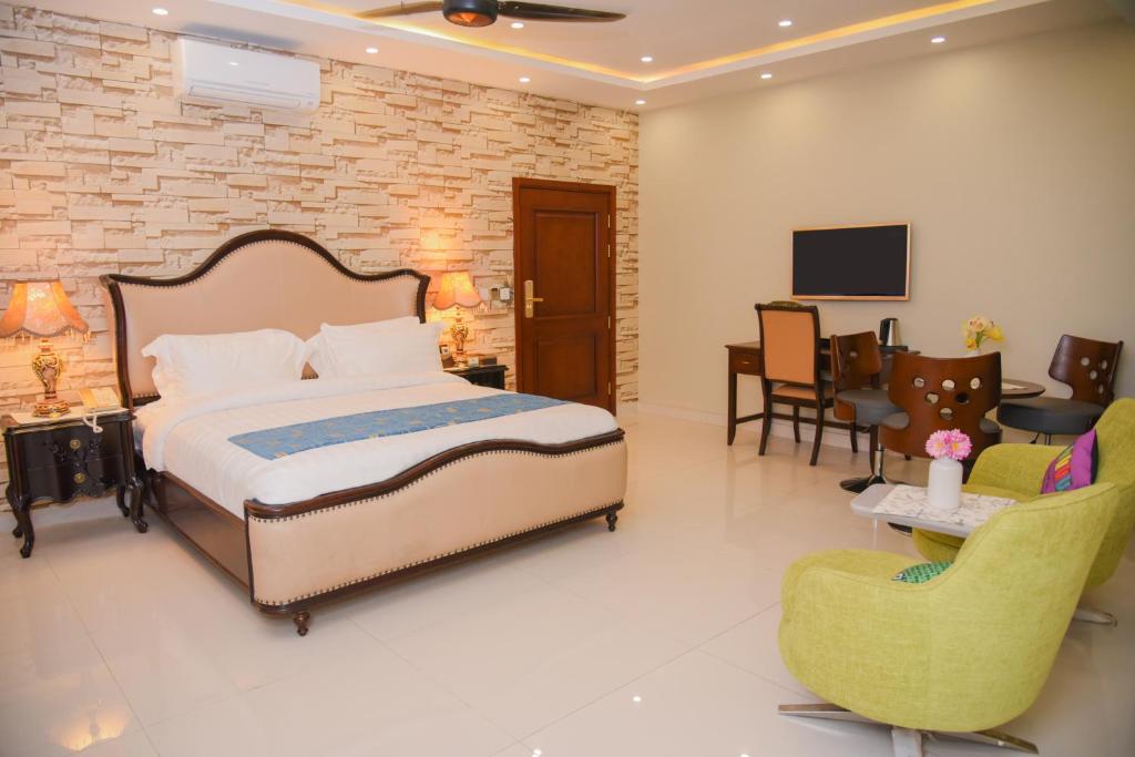 a bedroom with a bed and chairs and a tv at Orchards Cottage Hotel in Karachi