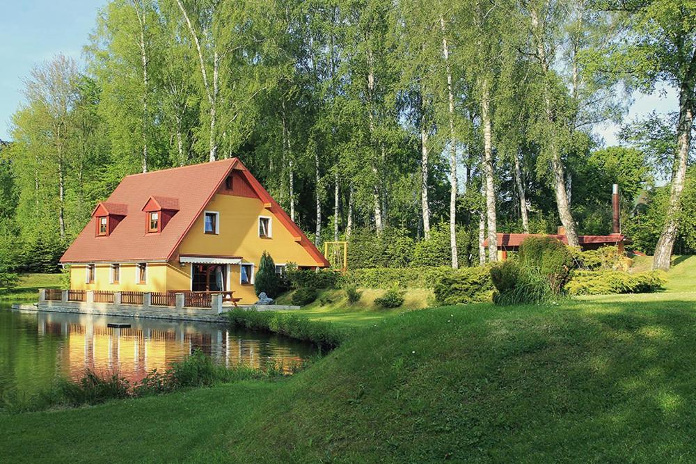 クラースナー・リーパにあるChalupa U rybníčkuの川の横に赤い屋根の黄色い家
