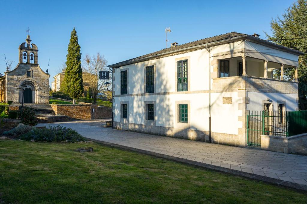 an old white building with a church in the background at Hotel Pazo de Berbetoros in Portomarin