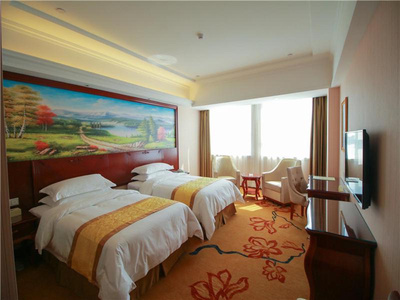 een hotelkamer met 2 bedden en een schilderij aan de muur bij Vienna International Hotel Shandong Weihai Rongcheng in Rongcheng