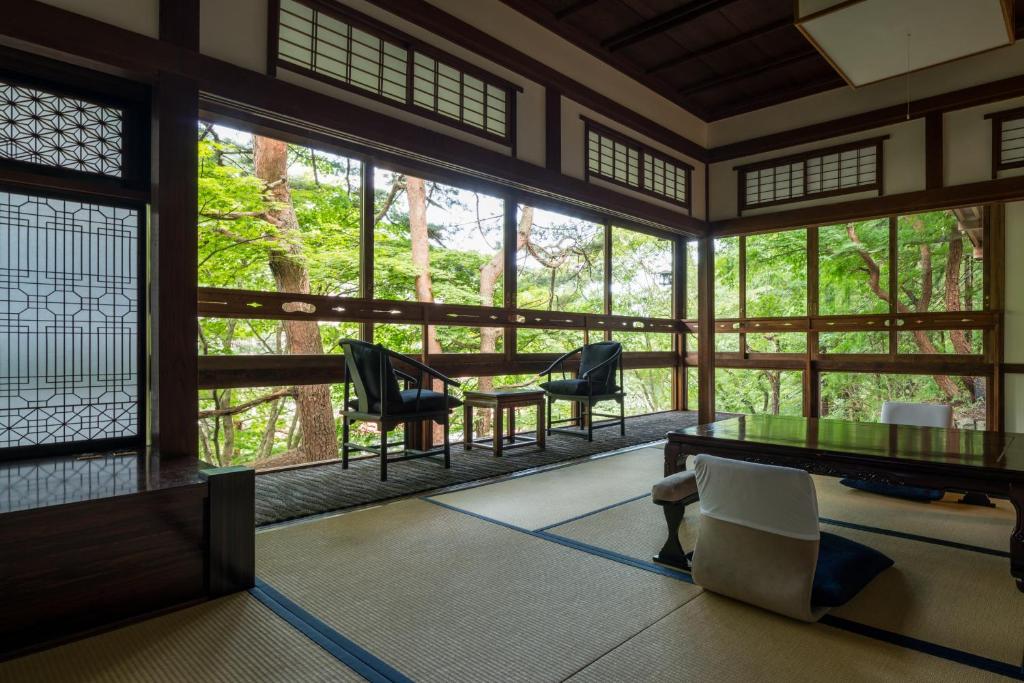 a room with a table and chairs and windows at Sekizenkan Kashotei Sanso in Nakanojo