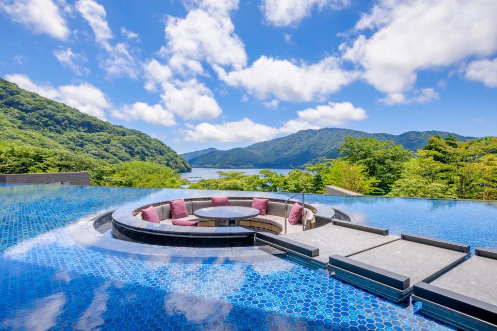 a infinity pool with a table and chairs and mountains at Hakone Ashinoko Hanaori in Hakone