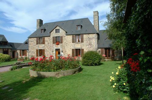 une grande maison en pierre avec une cour fleurie dans l'établissement Manoir De L'Acherie, à Sainte-Cécile