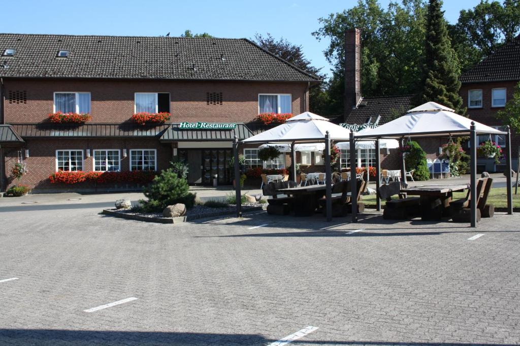 ein Parkplatz mit Tischen und Sonnenschirmen vor einem Gebäude in der Unterkunft Hotel König-Stuben in Bispingen