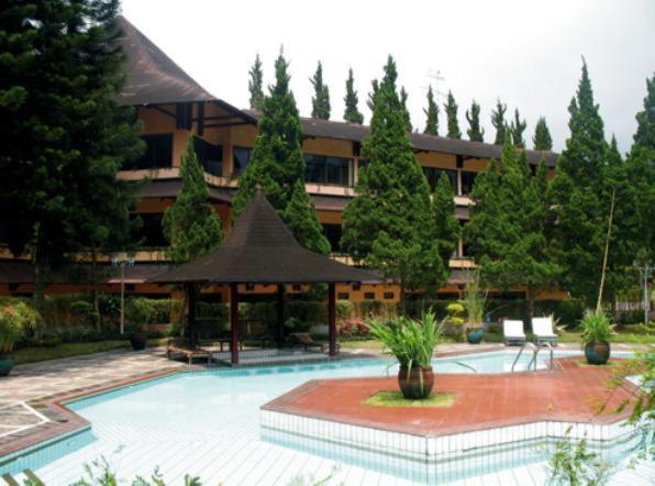 a large building with a swimming pool with a umbrella at Queen Garden Hotel in Baturaden