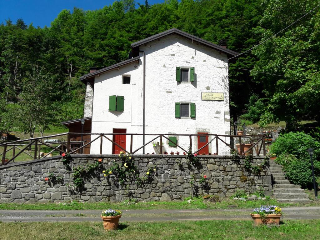 a white building with green shutters on a stone wall at B&B Boscoverde in Pievepelago