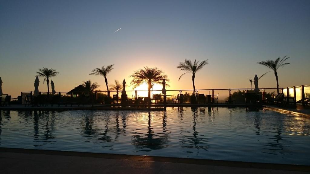 uma piscina com palmeiras e o pôr-do-sol ao fundo em Águas do Santinho Apart em Florianópolis