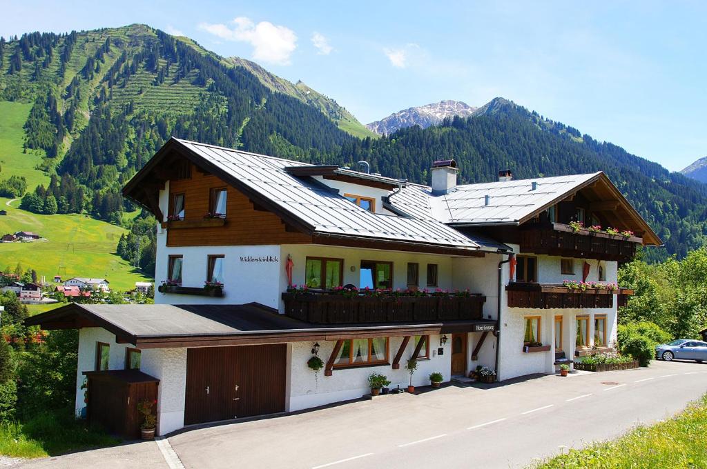 una casa en una colina con montañas en el fondo en Haus Widdersteinblick, en Riezlern