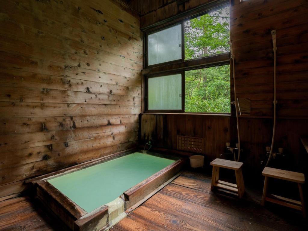 a room with a bed in a wooden room with two windows at Guesthouse Hoshizora no Akari in Matsumoto