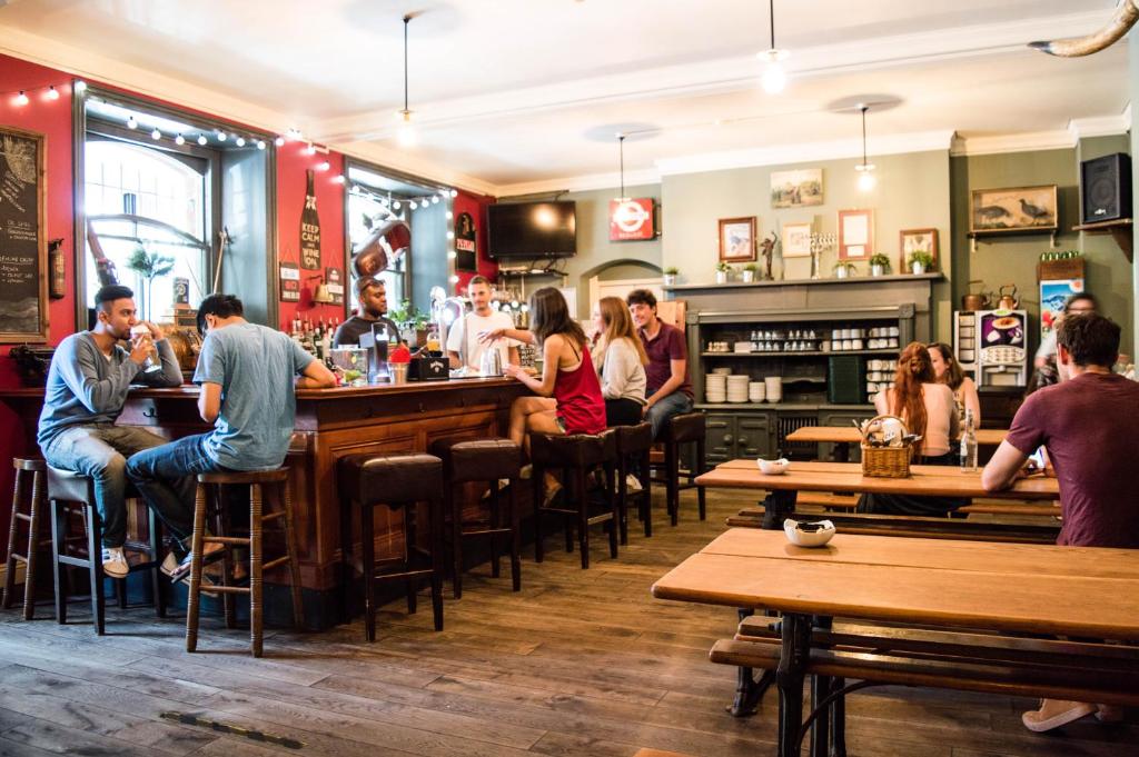 a group of people sitting at a bar in a restaurant at Palmers Lodge Swiss Cottage in London