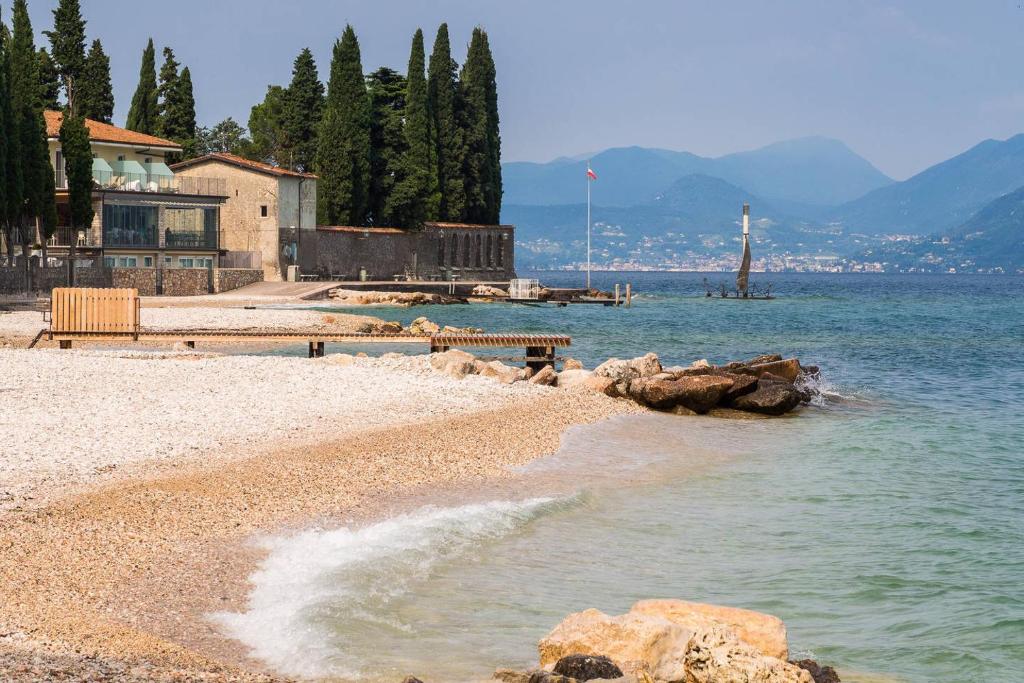 une plage avec des rochers dans l'eau et un bâtiment dans l'établissement Ortaglia A2, à Torri del Benaco