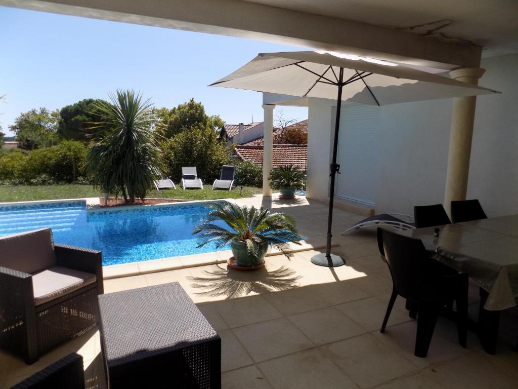 a patio with an umbrella and a swimming pool at Coté piscine Villa plain pied in Alignan-du-Vent