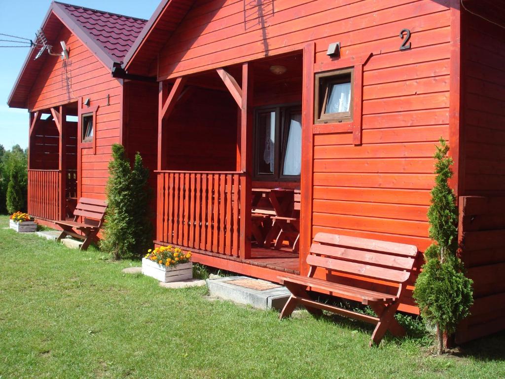 a red cabin with a bench in the grass at Ośrodek Wypoczynkowy "Słoneczko" in Rusinowo