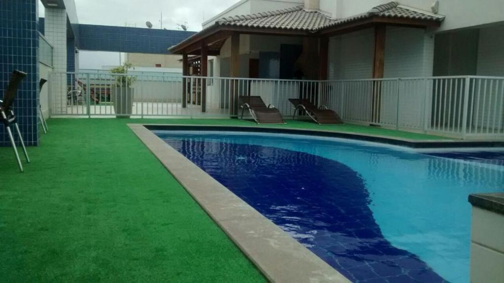 a swimming pool with green grass next to a house at Apto Praia de Itapoã 2 qto c/ar in Vila Velha