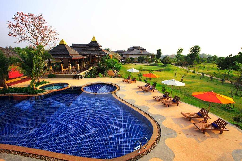 a swimming pool with tables and umbrellas in a resort at Mae Jo Golf Resort & Spa in San Sai