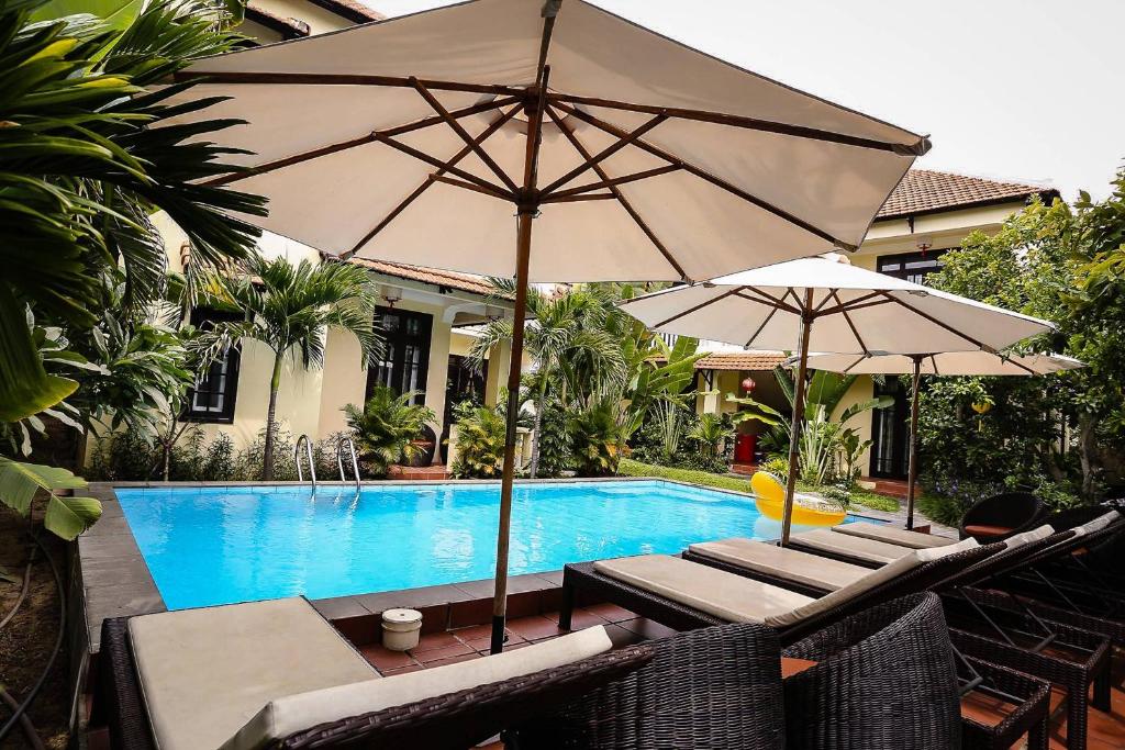 una piscina con 2 sombrillas y sillas junto a una piscina en Hoi An Holiday Villa, en Hoi An