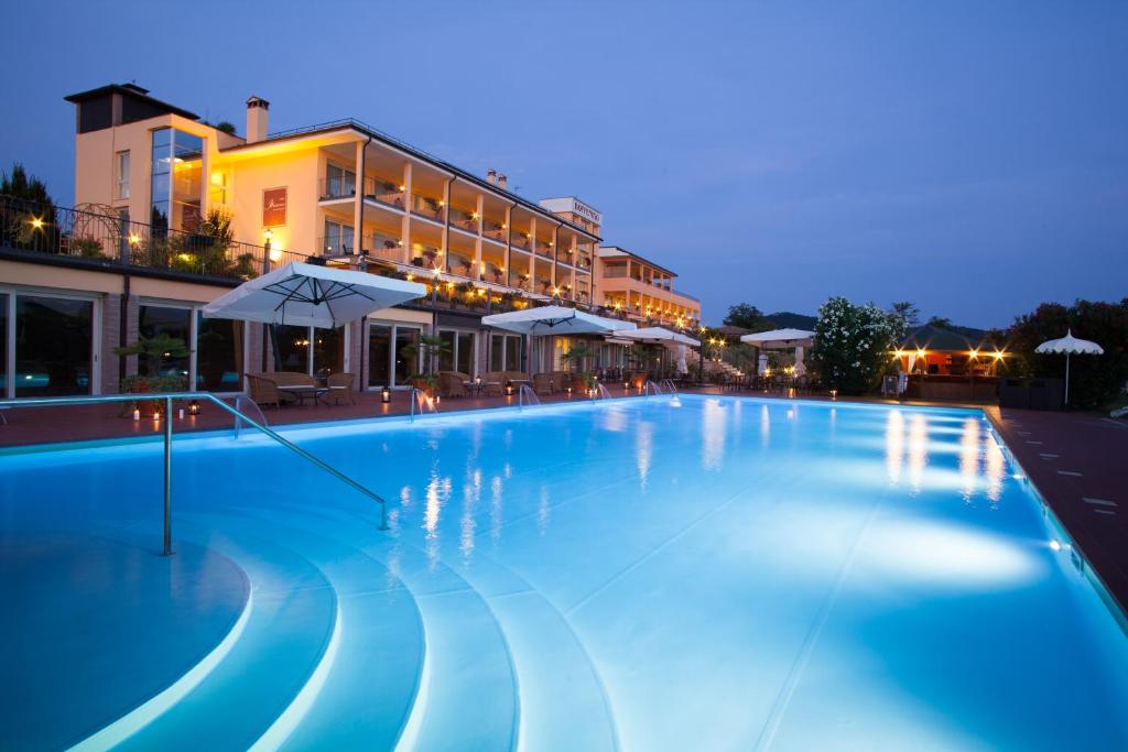 una gran piscina azul con sombrillas por la noche en Boffenigo Panorama & Experience Hotel, en Costermano