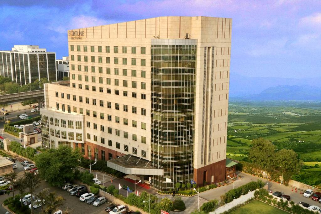 ein hohes Gebäude in einer Stadt mit Autos auf einem Parkplatz in der Unterkunft Fortune Select Global, Gurugram - Member ITC's Hotel Group in Gurgaon