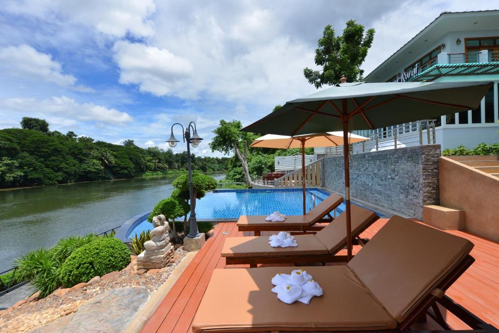 a pool with tables and umbrellas next to a river at Princess River Kwai Hotel in Kanchanaburi