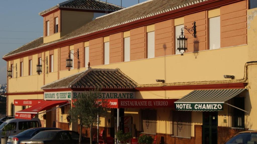 un grand bâtiment avec des voitures garées devant lui dans l'établissement Hotel Chamizo, à El Arahal