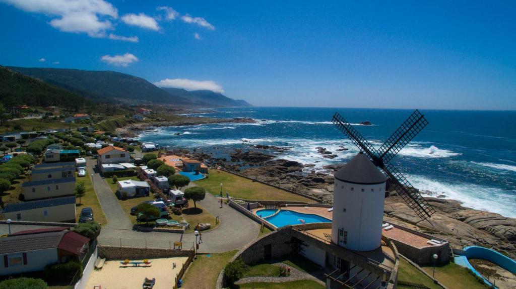 a windmill next to a beach with the ocean at Camping 1ª O Muiño - Bungalow Park in Oia