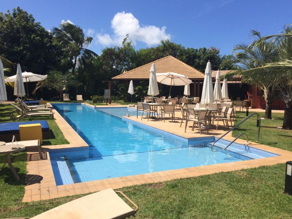 einen Pool mit Tischen, Stühlen und Sonnenschirmen in der Unterkunft Apartamento 2 suítes em condomínio de luxo no centro in Praia do Forte