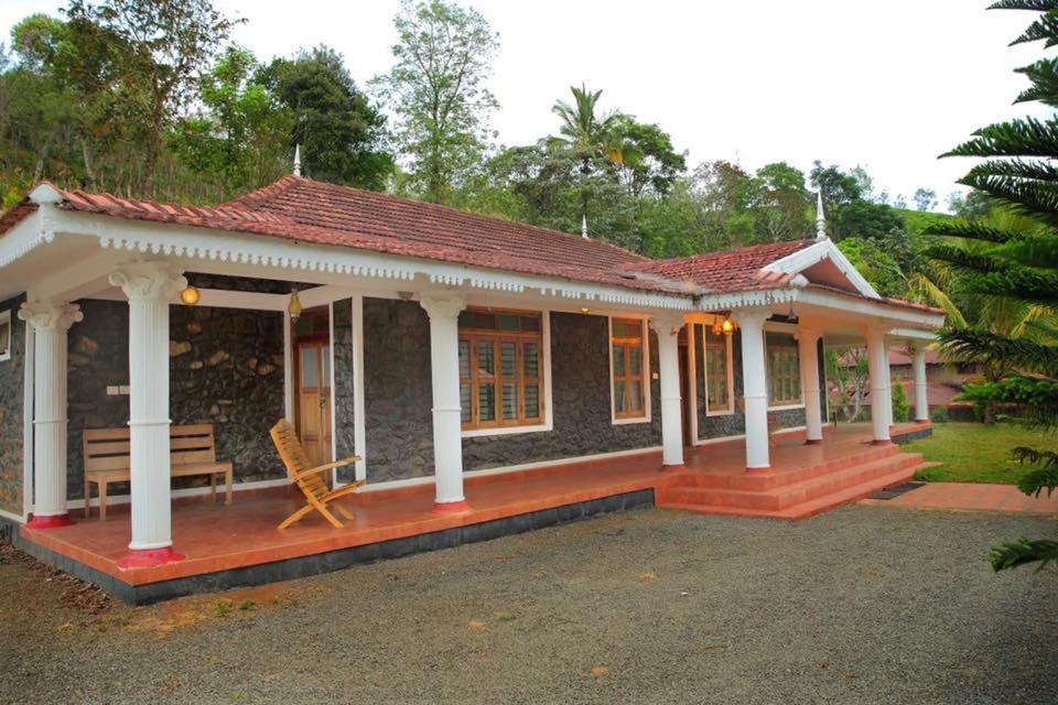 una casa con un porche y un banco frente a ella en Cassells Jungle Resorts Thekkady, en Vandiperiyār