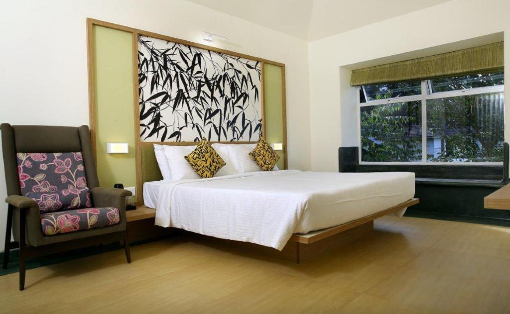 a bedroom with a bed and a chair and a window at Sterling Wayanad in Sultan Bathery